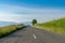 Empty blacktop highway in the countryside leading through green grass meadows to mountains in the background