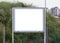 Empty and blank metallic information board to put what ever you want with a green grass hill in the background