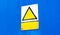 Empty blank real metal plate sign with a worn yellow warning triangle with symbol space and a text box, blue background, angle