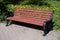 Empty brown wooden bench on black metal bases in the park against green lawn with dandelion flowers in sunny day