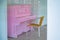 Empty chair in front of a pink piano