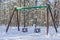 Empty childrens swing on a playground in a snowy winter park