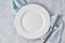 Empty clean white circle plate on grey linen tablecloth background with silverware