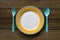 Empty color plate, fork and spoon on wooden table background