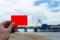 Empty coral - red plastic card in a man`s hand. The blurred background is a sea coast in England. Template for travel or holiday