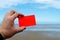 Empty coral - red plastic card in a man`s hand. The blurred background is a sea coast in England. Template for travel or holiday