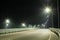 An empty country road with bumpers at the edges, lit by streetlights