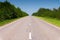 Empty country road on a summer day with green plantings of forest and greenery on the sides