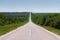 Empty country road on a summer day with green plantings of forest and greenery on the sides