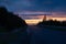 An empty countryside highway and some evergreen trees at dusk.