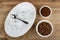 Empty cups, spoon in dish, bowl with roasted coffee beans, bowl with ground coffee on wooden table. Top view