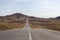 Empty curved cracked asphalt road to Lake Baikal is among the mountains with clear sky and dry grass.