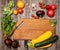 Empty cutting board and vegetables on weathered wooden background. Colorful ingredients for cooking on rustic wooden table around