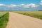 Empty dirt road through the fields. Fluffy clouds on a warm summer Sunny day over a field of wheat. Pure nature away from the big