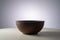 Empty earthen deep bowl on white table isolated on gray studio background. Brown handicraft ramekin or rustic plate