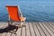 empty foldable beach chair on wooden deck overlooking calm water lake