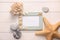 Empty frame with sea shells, starfishes and stones on white wooden background