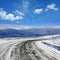 Empty frozen asphalt road and snow covered landscape with mountain over blue sky in winter time