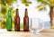 Empty goblet and bottles of beer on wooden table on blurred vacation background, craft cider and beer