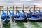 Empty gondolas docked between wooden mooring poles covered in tarpaulin in rainy November season in Venice, Italy