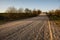 Empty gravel road in countryside in perspective with trees in surroundings. Summer colors.