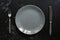 Empty gray plate and vintage fork and knife, black stone background. Top view