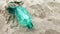 An empty green plastic bottle discarded on a beach. Coastal pollution