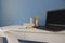 Empty home office of creative entrepreneur with black laptop on white table during lunch break. Modern workspace with blue cup of
