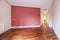 Empty living room with reddish parquet flooring with a wine red painted wall and a hallway with wardrobes