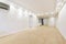 Empty living room with white walls, newly installed laminated floors, kitchen in the background and white access door