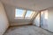 Empty mansard room with skylight windows under construction. Plaster walls. New home. Concrete walls. Interior renovation