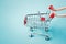 Empty miniature shopping cart with doll`s hand on grunge blue background , business and finance concept