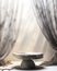 Empty minimal round gray marble podium side table in soft white blowing sheer cloth curtain drapery in sunlight for luxury