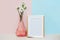 Empty modern golden white photo frame against pink blue background with white flower in pink vase on table. Moke up