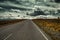 Empty mountain road goes into the distance beyond the horizon where the clouds are gathering.