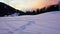 Empty moving cableway lift chairs on the snowy ground and trees at sunset