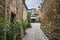 Empty narrow alley with potted plants between old rough weathered stone buildings on a sunny day