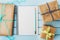 Empty notebook, pencil and gift or present box packed in kraft paper on blue wooden table