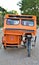 An empty orange tricycle is parked at the side of a road