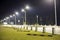 Empty parking lot on green lawn brightly illuminated by street lamps along road on dark night sky copy space background