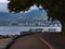 Empty paved footpath at the shore of Stanley Park, Canada below trees with rest benches and the city of West Vancouver.