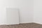 Empty picture frame canvas leaning against white wall in bright room with wooden floor with copy space - portfolio, gallery or