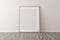 Empty picture frame leaning against white wall in bright room with wooden floor with copy space - portfolio, gallery or artwork