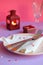 Empty pink plate, cutlery, hearts, candlesticks, wine glasses and red gift on pink-purple background. St. Valentine`s Day table