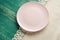 Empty pink plate on tablecloth on wooden table. Top view.