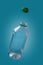 Empty plastic bottle with water drops and green cover levitating on blue background