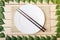 Empty plate on a bamboo mat with chopsticks, top view, on a wooden background, framed with leaves of a tree