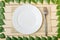 Empty plate on a bamboo mat with a fork, view from top, on a wooden background, framed with leaves of a tree