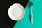 Empty plate and fork on turquoise and black background.