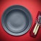 Empty plate on a red background table with a knife and fork. Festive tableware for a festive dinner